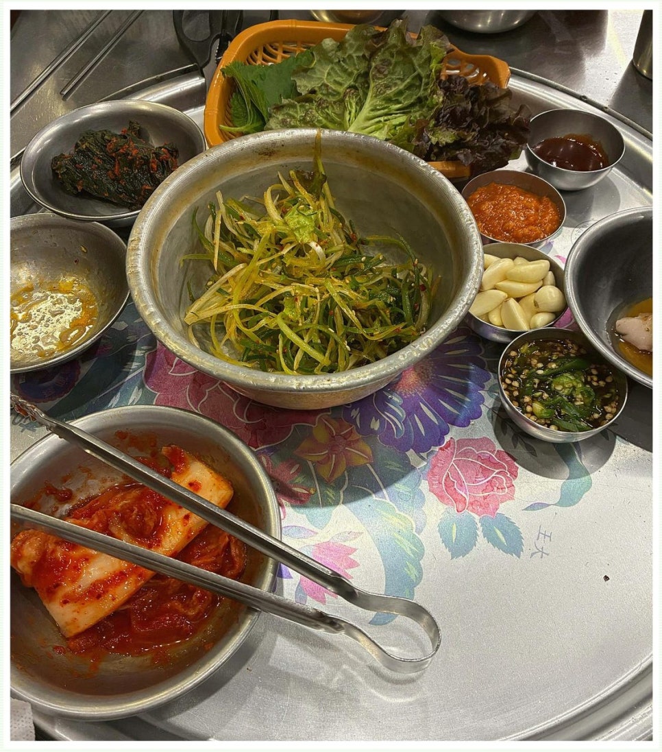 파절이와 배추김치, 상추·깻잎 쌈채소, 쌈장과 마늘, 절임 소스류가 스테인리스 그릇에 담겨 나온 고기 상차림
