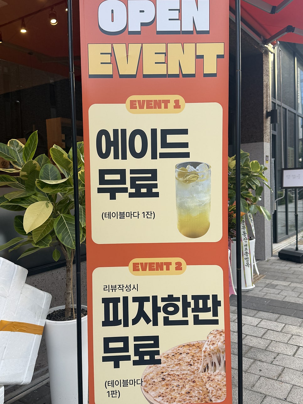 입구에 세워진 오픈 이벤트 배너 — 에이드 무료, 리뷰 작성 시 피자 한 판 무료 안내