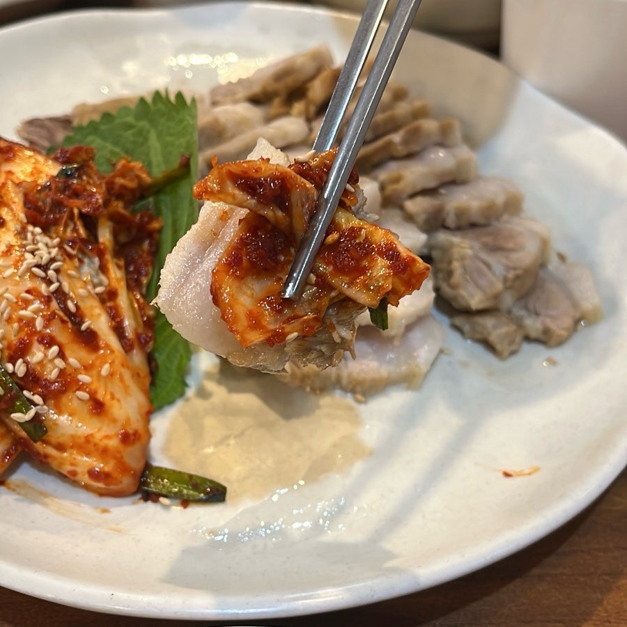 수육 한 장에 보쌈김치를 올려 한입 크기로 집어 든 모습