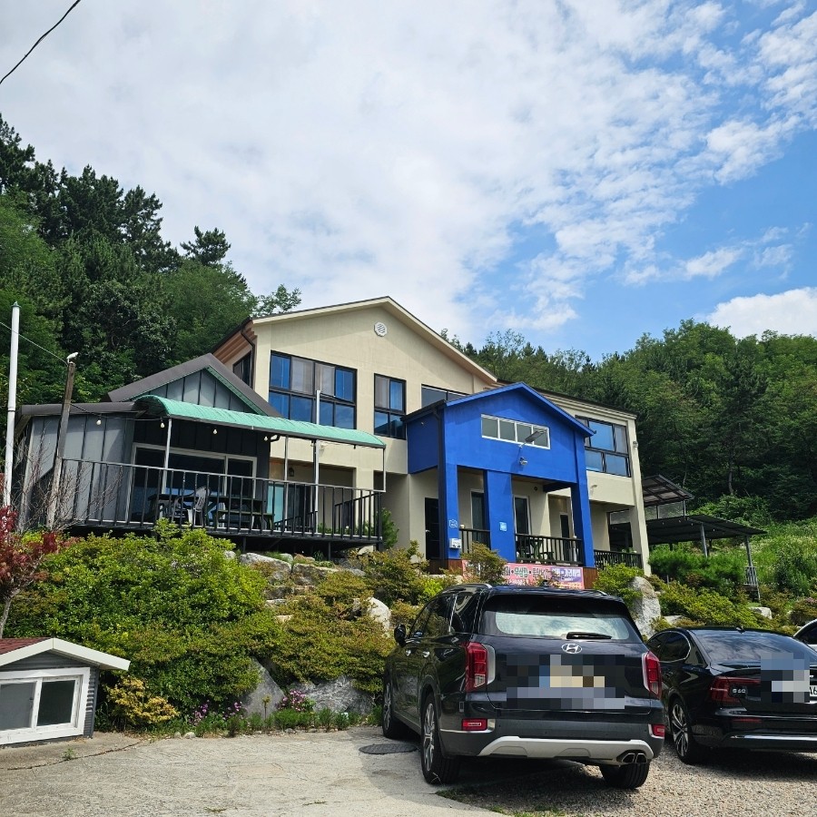 파란 포인트가 들어간 동해펜션 외관과 마당 주차 공간.