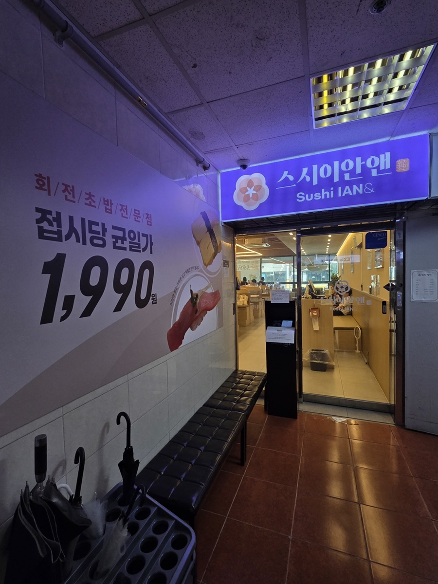 2층 매장 입구. 왼쪽 벽면에 균일가 안내가, 앞쪽에는 대기용 벤치와 우산 정리함이 놓여 있다.