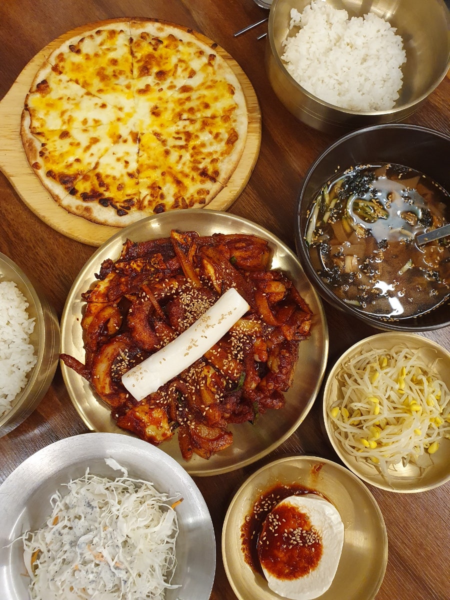 가래떡이 올라간 낙지볶음과 고르곤졸라피자, 연두부·콩나물·양배추 샐러드 반찬.