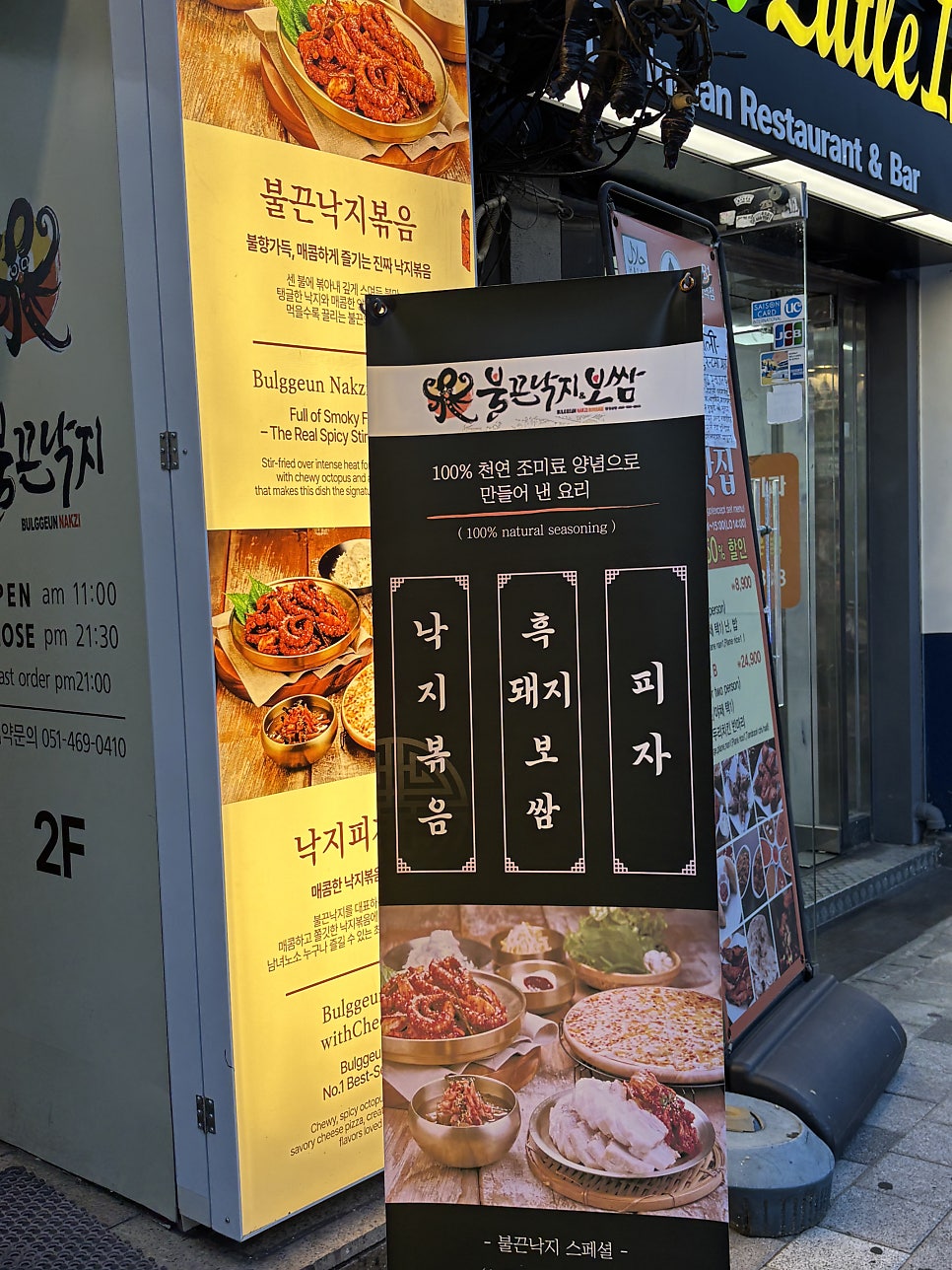 입구 앞 배너에 적힌 낙지볶음·흑돼지보쌈·피자 구성과 영업시간 안내.