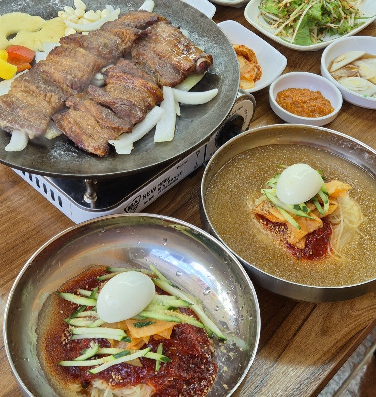 버너 위에 채소와 함께 구워져 나온 양념돼지갈비와 밀면 두 그릇