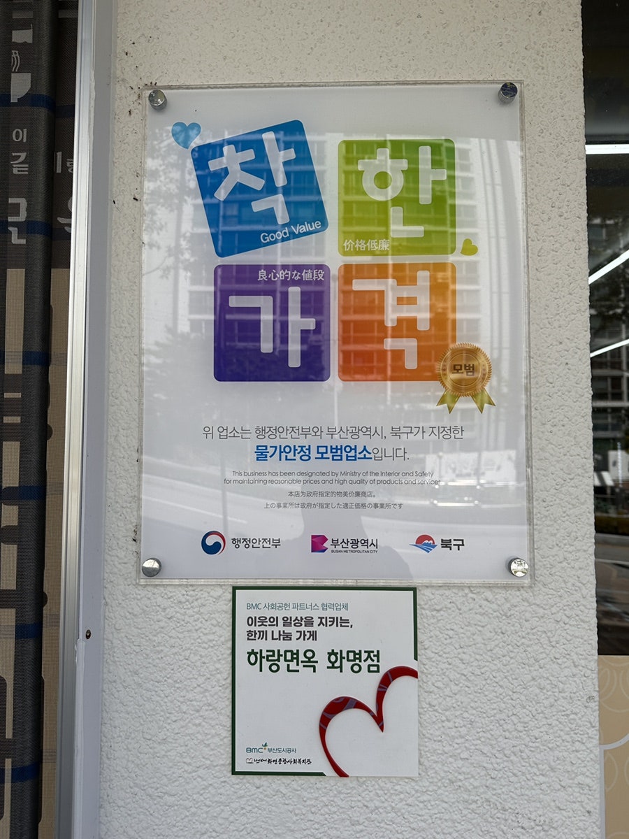 입구 벽에 붙은 물가안정 모범업소 '착한가격' 인증판과 한끼 나눔 가게 스티커