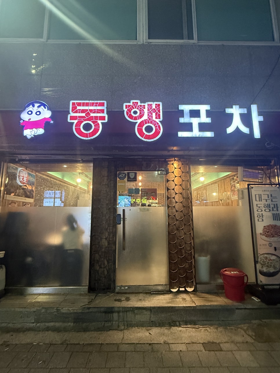 밤에 조명이 켜진 동행포차 구포본점 정면 — 안쪽으로 손님들이 보인다