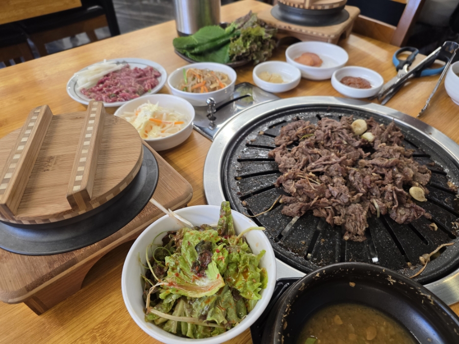 상추겉절이, 잡채, 양배추샐러드와 쌈채소가 깔린 넓은 테이블과 숯불 불판