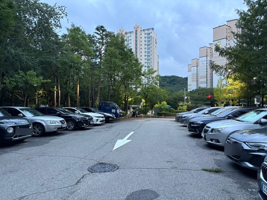 저녁 무렵 차량이 들어선 넓은 주차 공간과 주변 아파트 전경