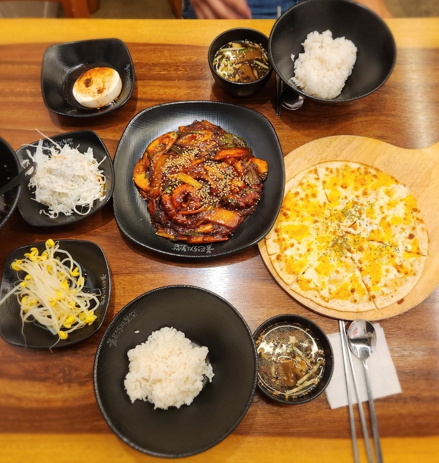 낙지피자세트 2인 상차림. 낙지볶음과 고르곤졸라피자, 공기밥, 양배추샐러드·콩나물·연두부·묵사발이 함께 나옵니다.
