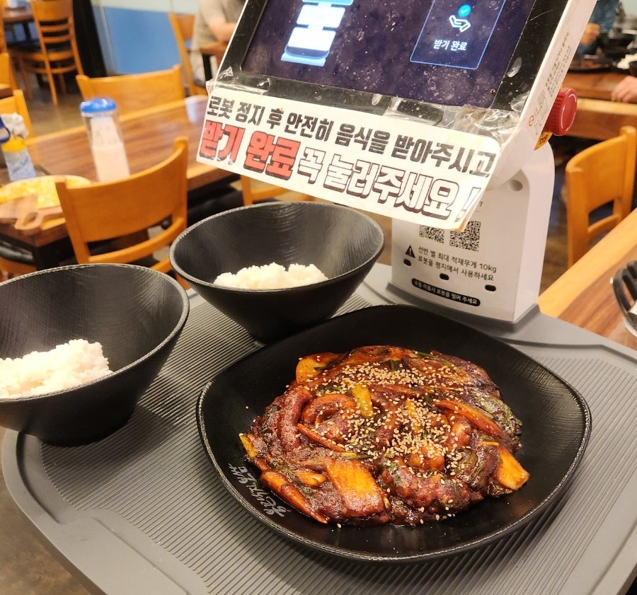 서빙로봇이 낙지볶음과 공기밥을 테이블까지 가져다줍니다. 받은 뒤 '받기 완료'를 눌러달라는 안내가 붙어 있습니다.