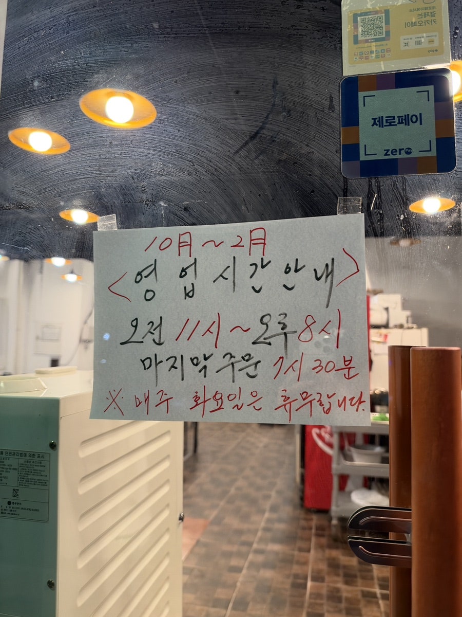 출입문에 붙은 손글씨 영업시간 안내. 마지막 주문 시간과 화요일 휴무가 적혀 있습니다.