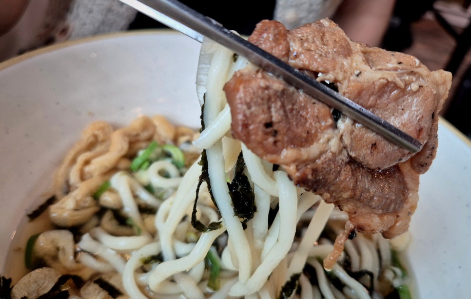 쫄깃한 우동 면 위에 돼지불고기 한 점을 올려 집어 든 모습.